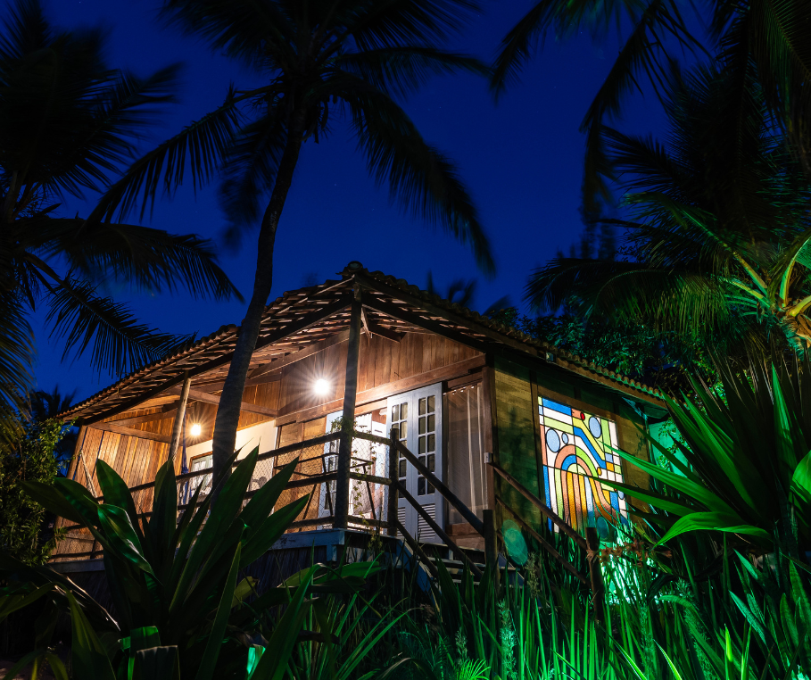 Bangalô Memórias – exterior noturno com vitrais iluminados entre coqueirais
